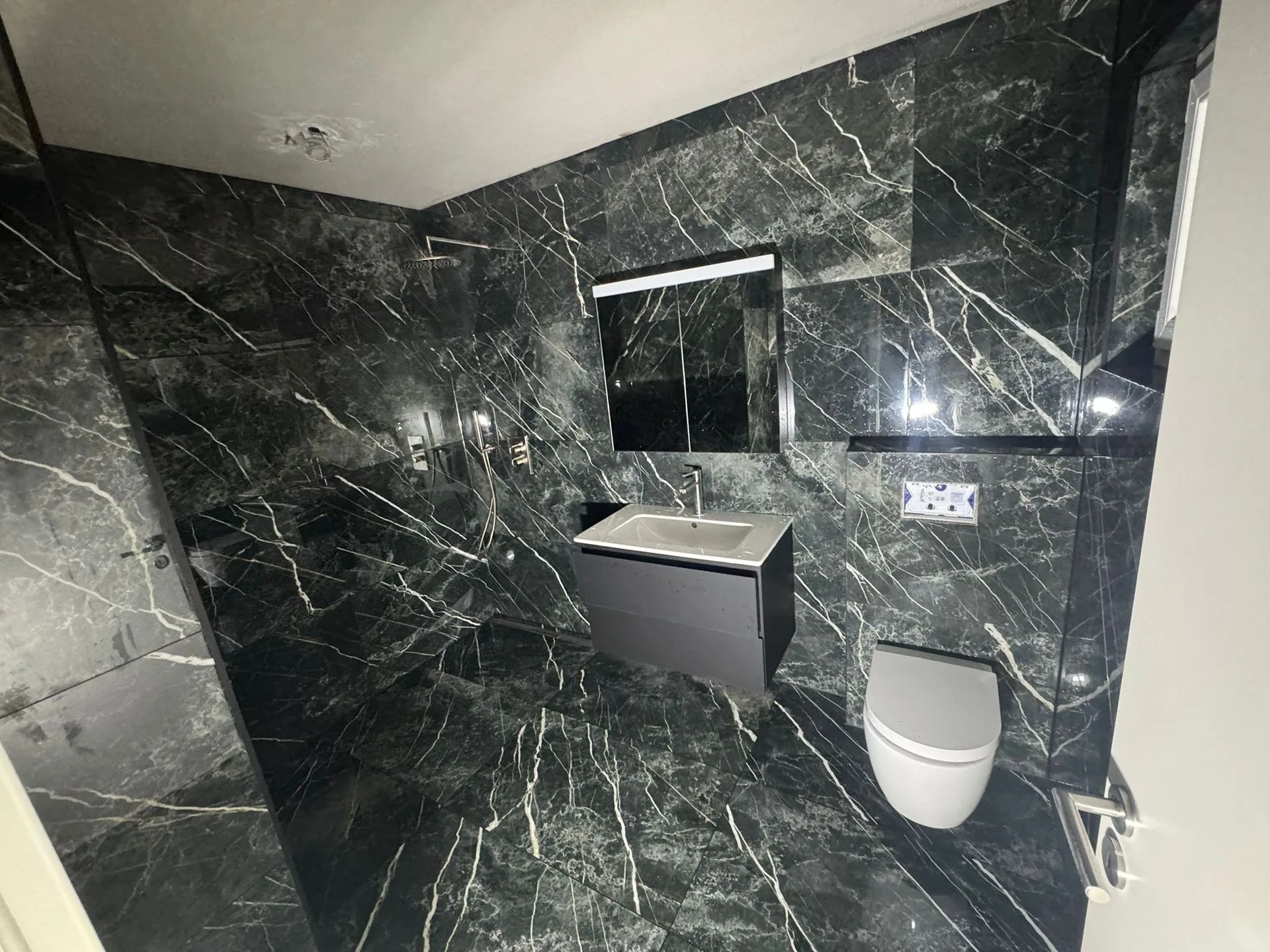 Salle de bain en marbre noir avec douche vitrée, rénovation premium réalisée par BNG Rénovation sur l'arc lémanique