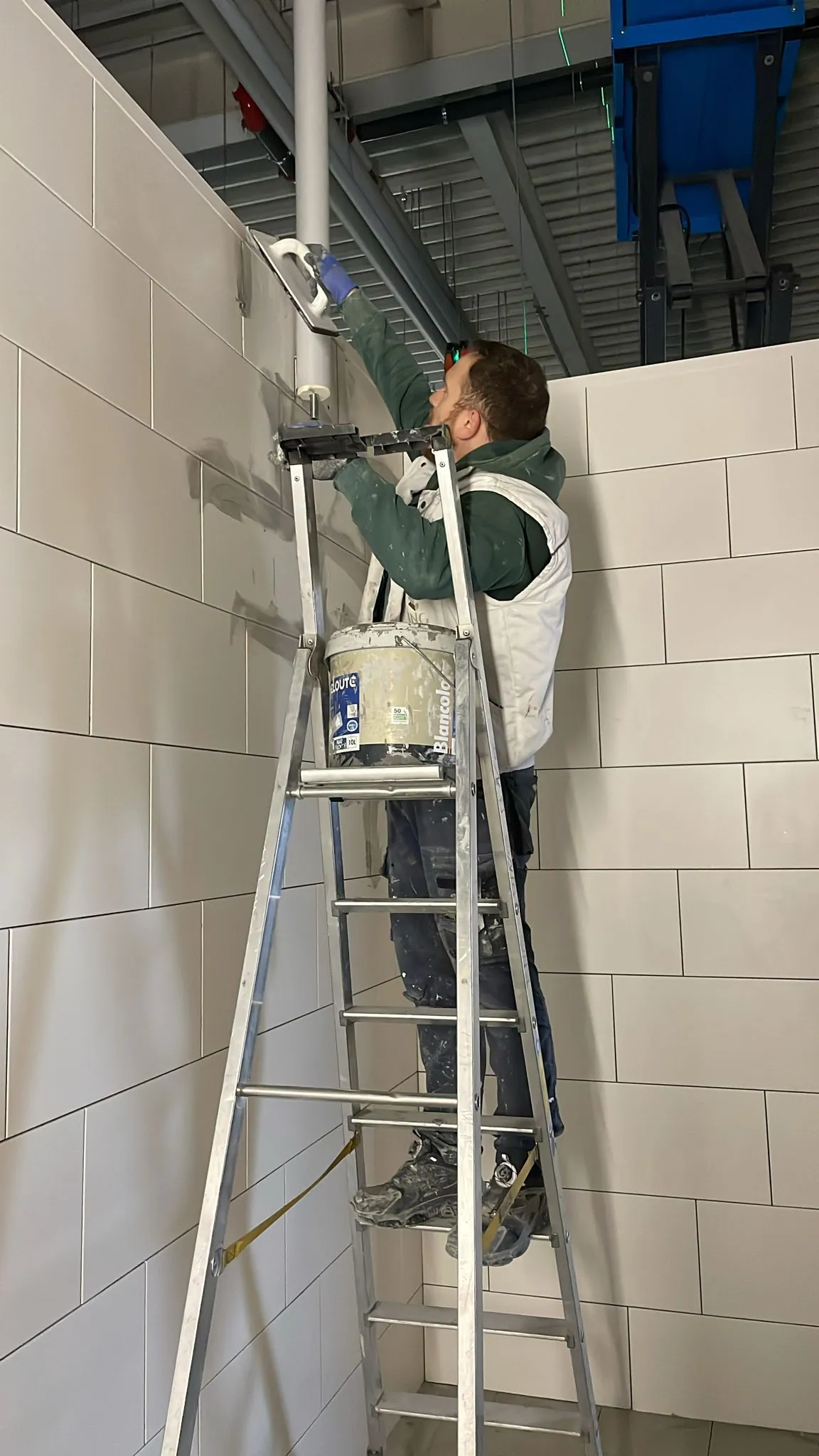 Peintre de BNG sur un escabeau, mur en blocs peint en blanc