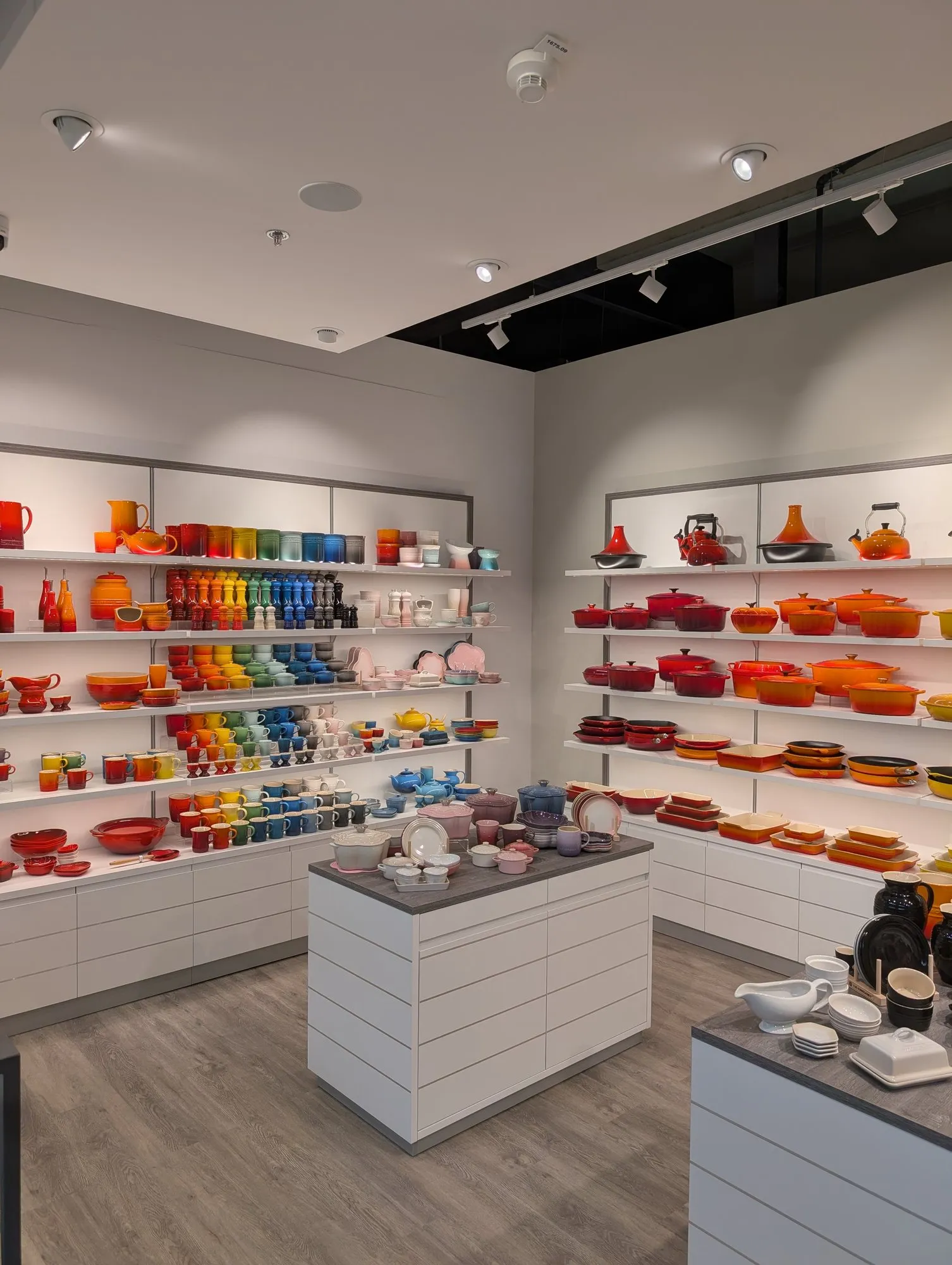Surface de vente de la boutique Le Creuset à Aubonne : étagères de cocottes colorées, îlots blancs, faux-plafond à spots et sol aspect chêne