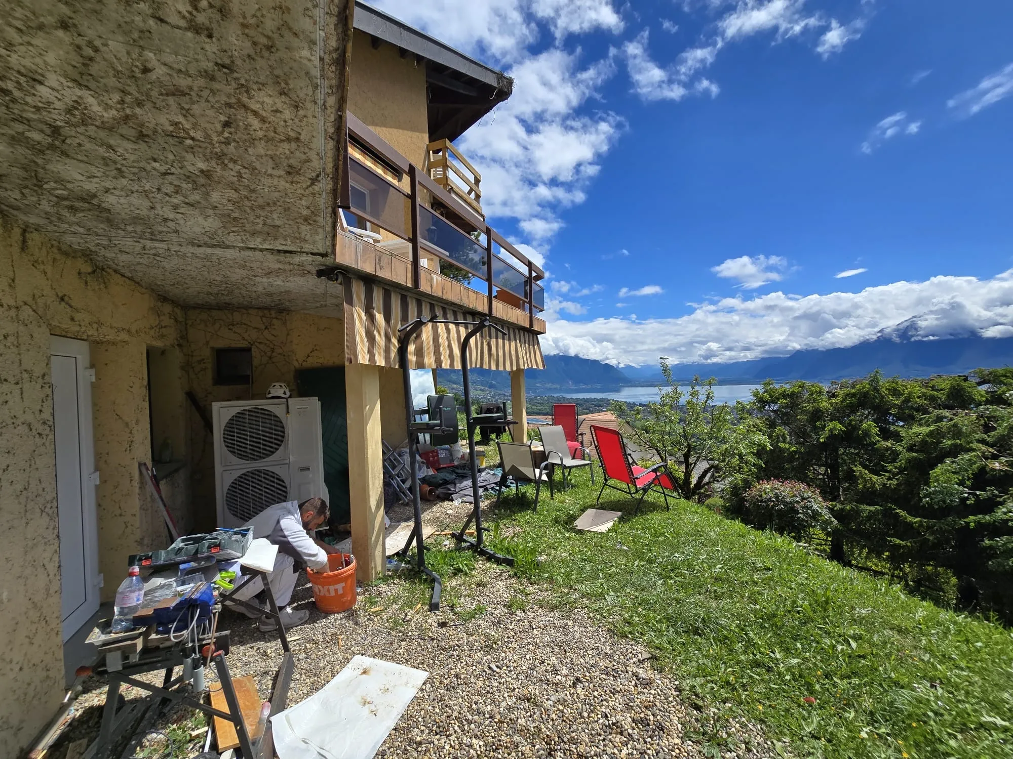 Le jardin en pente avant les travaux : terre, gravier et gazon devant la maison, vue sur le lac