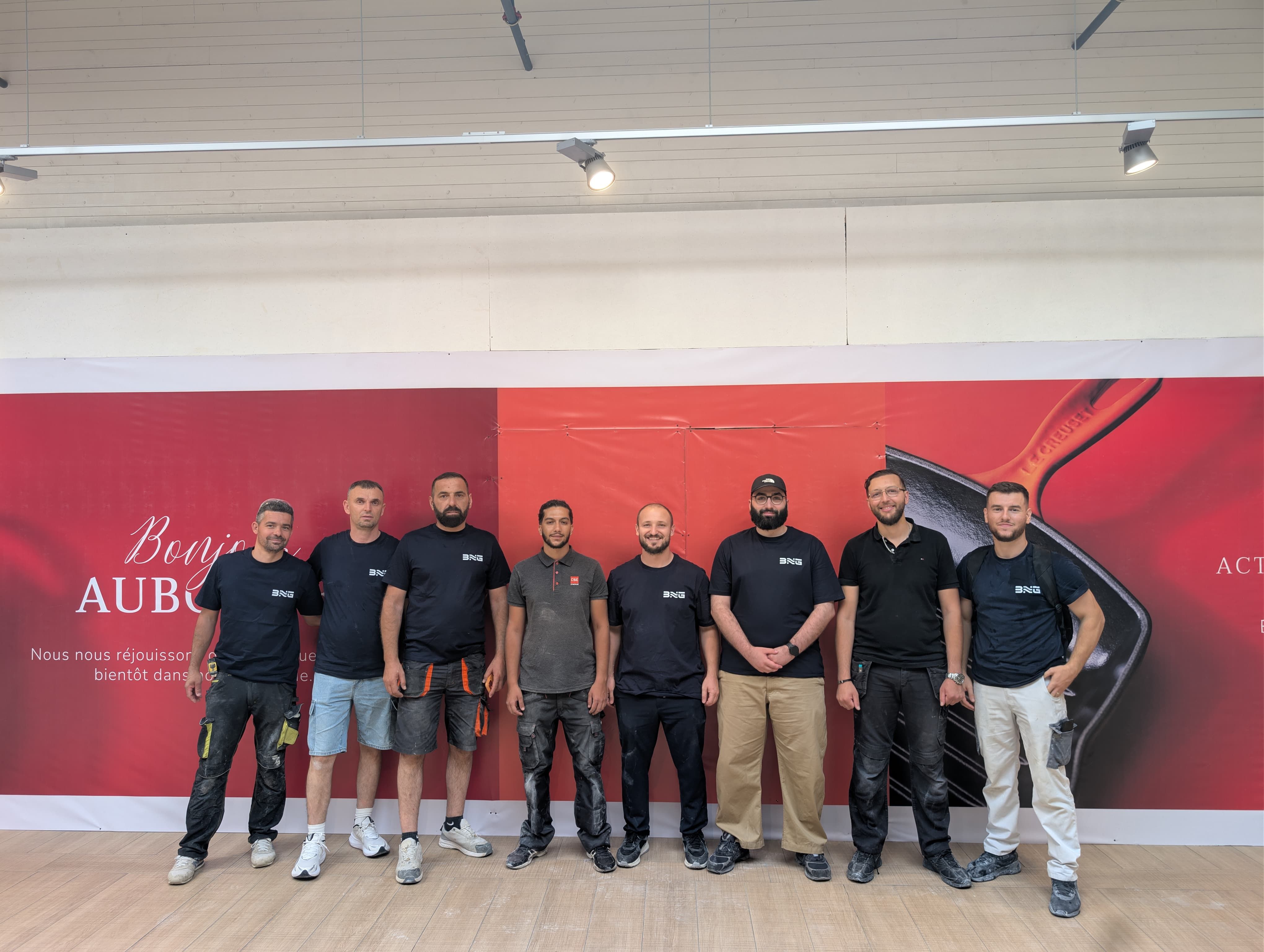 Les neuf personnes de l’équipe BNG Rénovation, en t-shirt noir au logo BNG, debout côte à côte sur un chantier