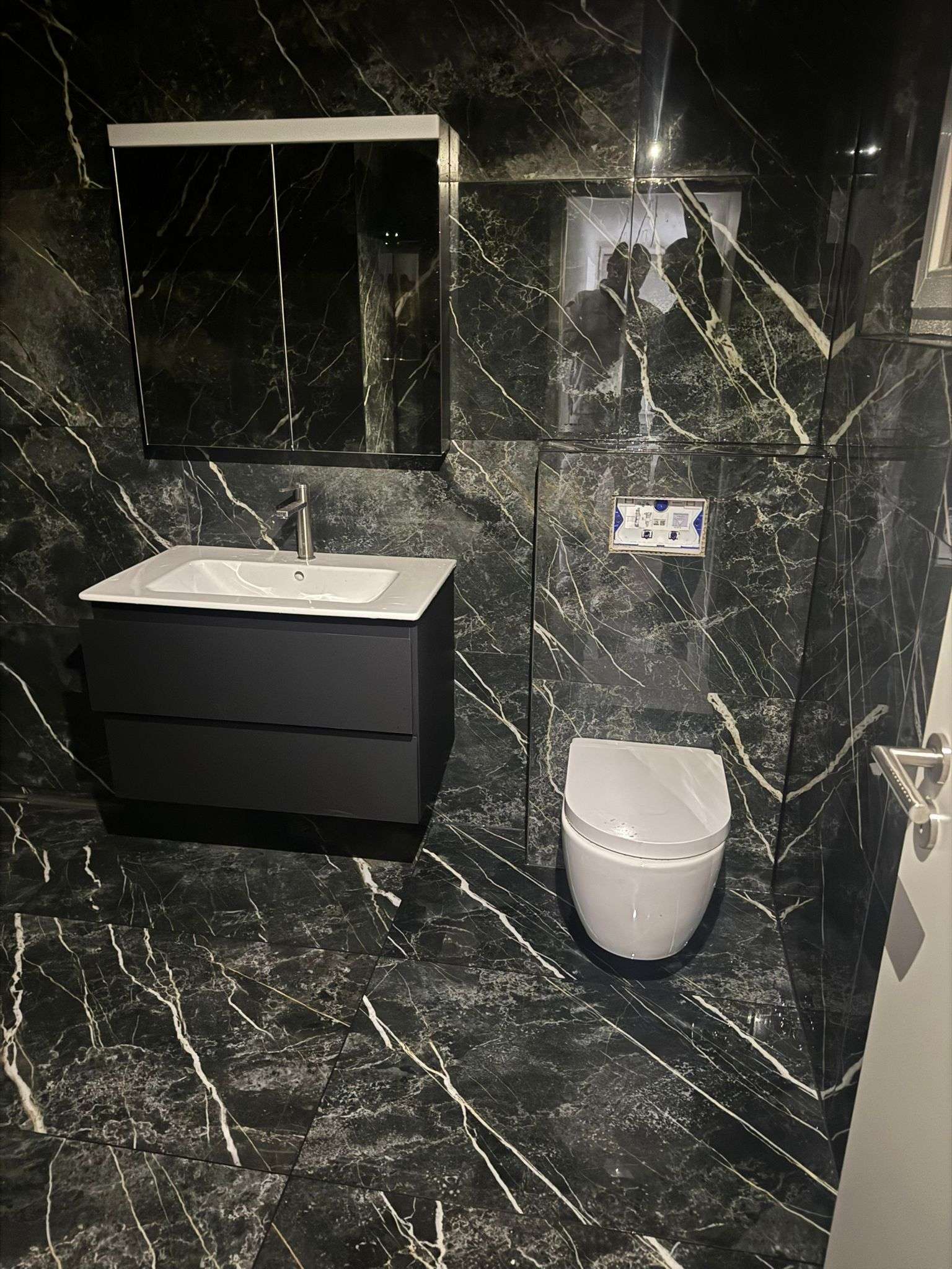 Salle de bain en marbre noir veiné, meuble vasque suspendu et WC suspendu, dans une villa à Corseaux